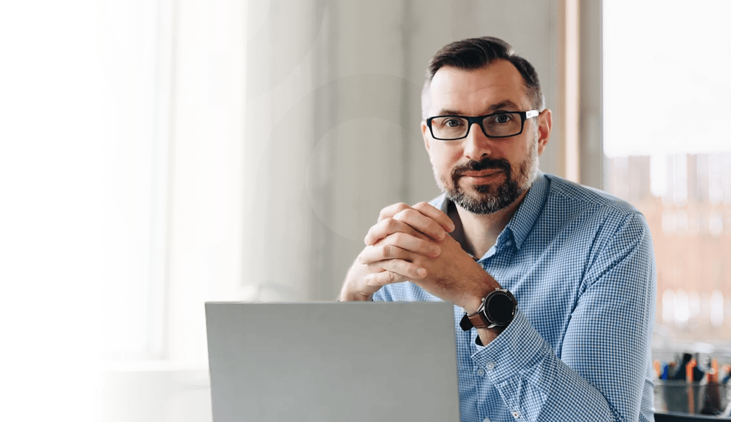 Man sitting at a desk with a laptop, looking at the camera