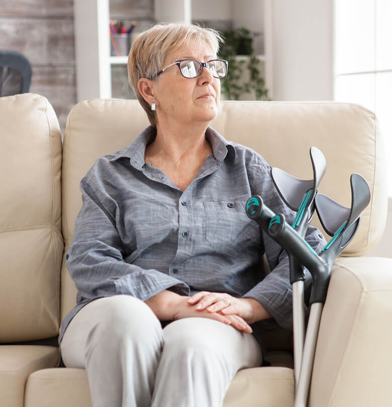 Elderly woman sitting on a couch at home with crutches beside her